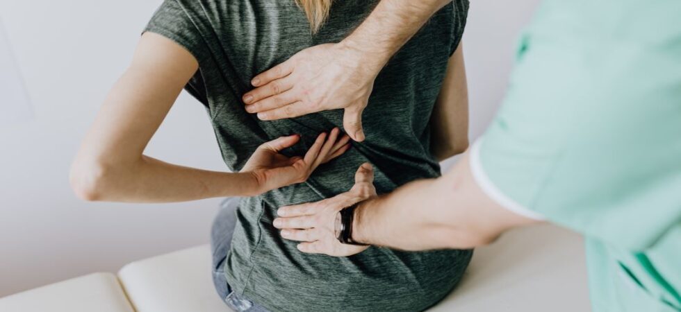 low back pain: a lady with low back pain sitting while getting examined by a person